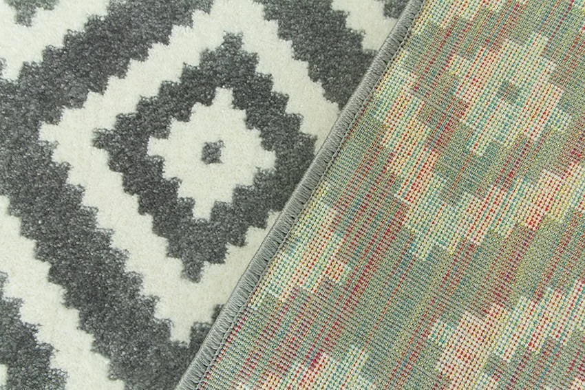 Spatele unui covor geometric modern gri si alb, cu margine festonata si materiale rezistente pentru utilizare indelungata.